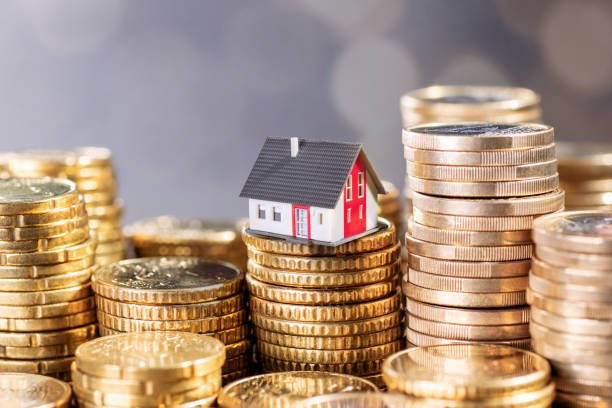 the cost of real estate. house with stacks of coins.